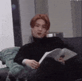 a man is sitting on a couch reading a book and making a funny face .