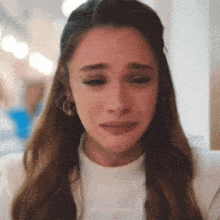 a woman is crying while wearing a white shirt and earrings