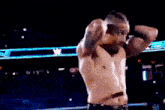 a shirtless wrestler is standing in a wrestling ring with his hands on his head .