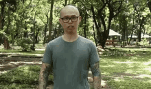 a man with glasses and tattoos is standing in a park