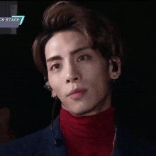 a man wearing a red turtleneck looks at the camera with a sign above him that says ck stage