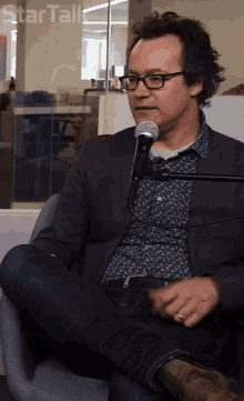 a man with glasses is sitting in front of a microphone with the words star talk below him