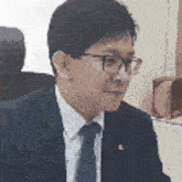 a man in a suit and tie is sitting at a desk with glasses .