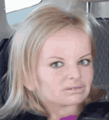 a woman with blonde hair is making a funny face while sitting on an airplane .