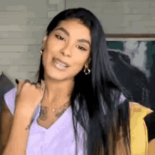 a woman with long black hair is wearing a purple shirt and earrings and is making a funny face .