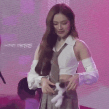 a woman in a crop top and tie is holding a stuffed animal in her pocket .