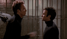 two men are standing next to each other in a jail cell and talking to each other .