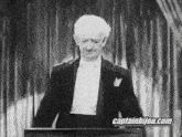 a man in a tuxedo and bow tie is standing in front of a podium .