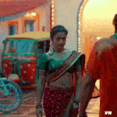 a woman in a red saree stands next to a man in an orange shirt
