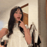 a woman wearing a white shirt has her finger on her chin