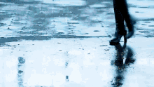 a person walking in the rain with their reflection in the puddles