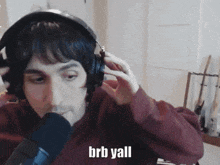 a man wearing headphones is talking into a microphone and the words brb yall are on the screen
