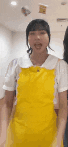 a woman wearing a yellow apron and a white shirt is standing in a room with her mouth open .