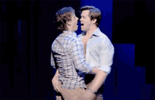 two men are hugging and kissing on a stage in front of a blue backdrop