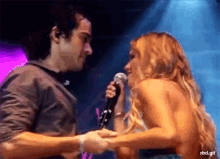 a woman singing into a microphone while a man holds her hands