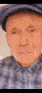 a close up of an older man 's face wearing a hat and a plaid shirt .