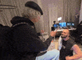 two men are sitting on the floor in a room talking to each other . one of the men is wearing a beret .