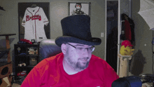 a man wearing a top hat and glasses is sitting in front of a braves jersey
