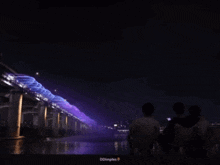 a group of people sitting in front of a bridge that is lit up at night