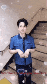 a young man in a blue shirt is standing in front of stairs with hearts around him