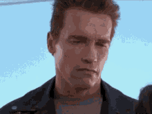 arnold schwarzenegger is wearing a leather jacket and a gray shirt and looking at the camera .