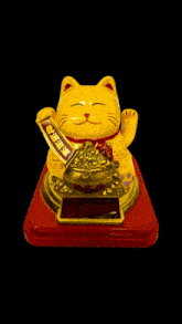 a yellow statue of a cat with chinese writing on it is sitting on a red base