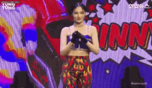 a woman in a crop top and flaming pants is standing in front of a large screen .