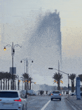 cars are driving down a street in front of a tall fountain