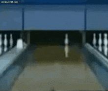 a blurred image of a bowling alley with bowling pins and a ball going down the alley .