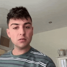 a young man wearing a striped shirt is looking at the camera .
