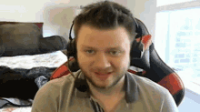 a man with a beard is wearing headphones and a microphone while sitting in a gaming chair .