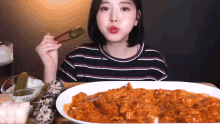 a woman in a striped shirt is eating a plate of food with chopsticks