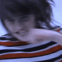 a blurry picture of a woman wearing a striped shirt with her hair blowing in the wind .