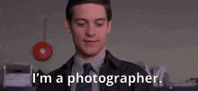 a man in a suit and tie is smiling and saying `` i 'm a photographer . ''