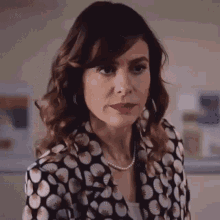 a woman wearing a polka dot shirt and a pearl necklace is standing in front of a washing machine .