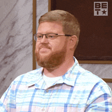 a man wearing glasses and a plaid shirt is standing in front of a be t logo