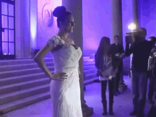 a woman in a white dress is standing in front of a purple wall