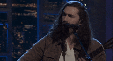 a man with long hair sings into a microphone while playing a guitar