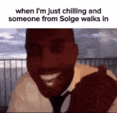 a man in a suit and tie is smiling while someone from solge walks in behind him