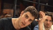 two men are sitting at a table with one holding something in his hand and the other looking at the camera