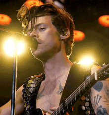 harry styles is singing into a microphone while playing a guitar