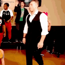 a man in a black vest and white shirt is dancing in front of a group of people