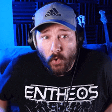 a man wearing headphones and an adidas hat is wearing a shirt that says entheos