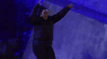 a man in a black jacket is dancing in a dark room with blue lights .