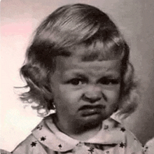 a black and white photo of a little girl with an angry face .