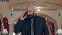 a bald man in a suit and tie talking on a cell phone