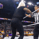 a man in a black shirt is standing in a wrestling ring holding a referee 's baton