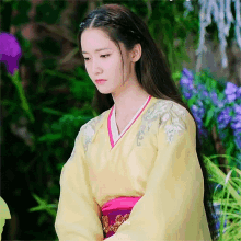 a woman in a yellow and pink kimono is sitting in front of purple flowers