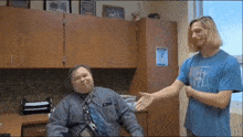a man in a blue t-shirt with the letter m on it is shaking hands with another man