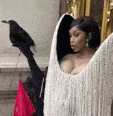 a woman in a white fringed dress holds a black bird on her arm